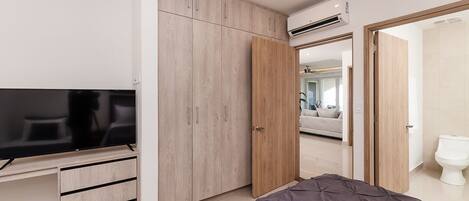 A modern bedroom with a bed, a TV, a wardrobe, and an air conditioning unit.