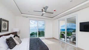 A modern bedroom with a bed, a ceiling fan, a large sliding glass door leading to a balcony, and a flat-screen TV mounted on the wall. - La Vista #B10, amazing Views - Brand New 3 bd Condo overlooking Tamarindo Bay Vista B-10 (Tamarindo)