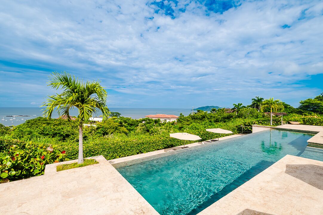 A swimming pool with a view of the ocean and lush greenery.