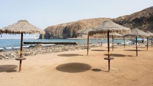 A beach with thatched umbrellas and rocky terrain.