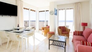 A bright living room with a glass table, a sofa, and a TV mounted on the wall.