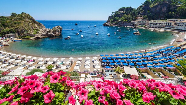 A coastal beach with numerous sun loungers and umbrellas, boats in the water, and a rocky landscape in the background. - Panoramic Taormina Center (Taormina)