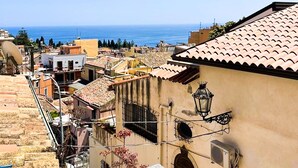 A coastal town with terracotta-roofed buildings, a clear blue sky, and the sea in the background. - Panoramic Taormina Center (Taormina)