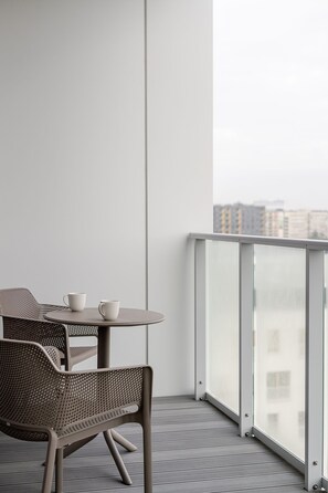 A balcony with a round table and two chairs, a view of buildings in the background, and a clear sky.