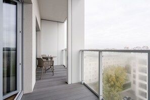 A balcony with a table and chairs, a view of buildings, and a glass door.