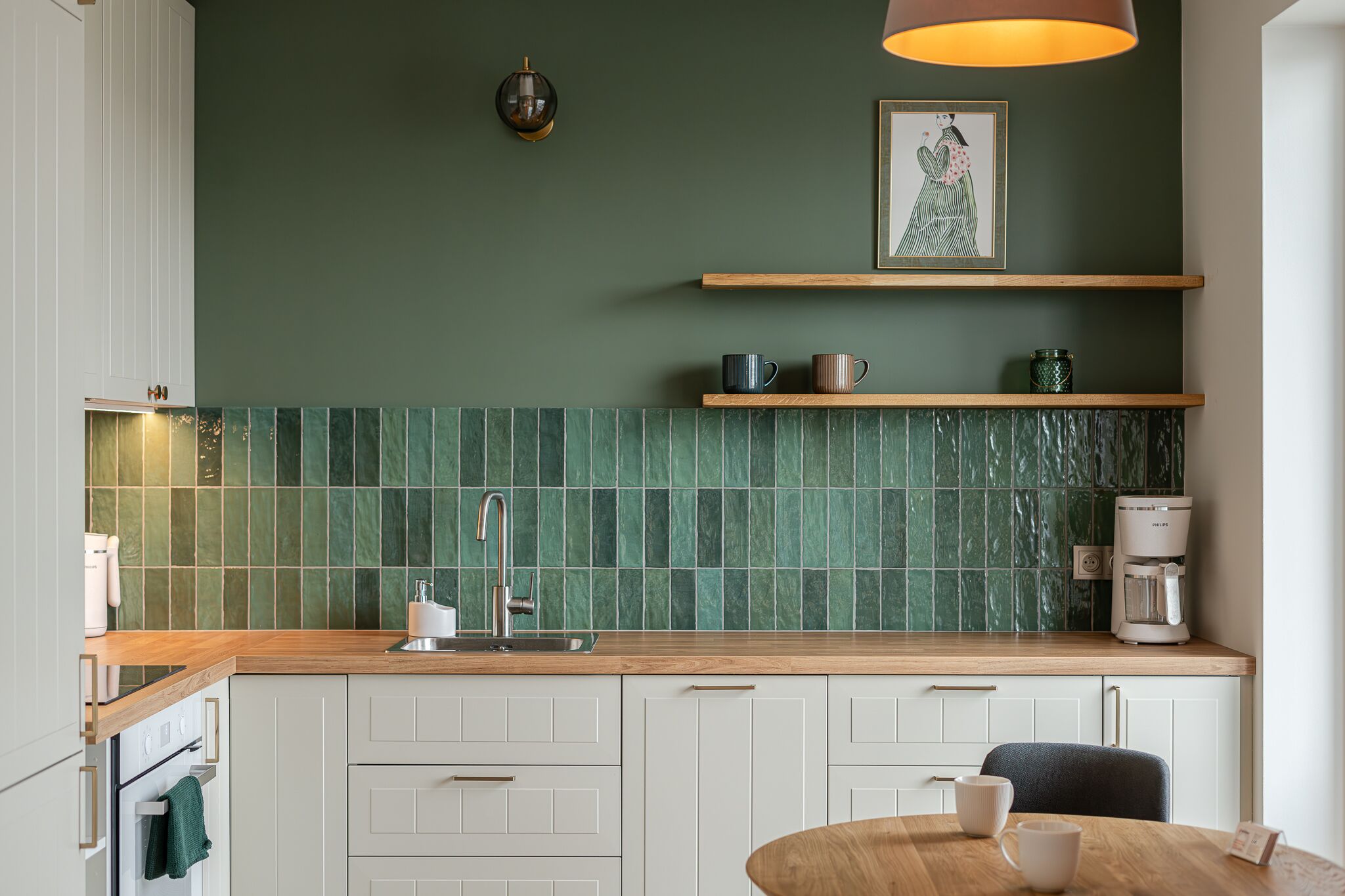 Una cocina moderna con azulejos verdes, repisas de madera y una cafetera.