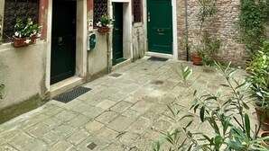 Un patio con un edificio rojo, una puerta verde y plantas en macetas.