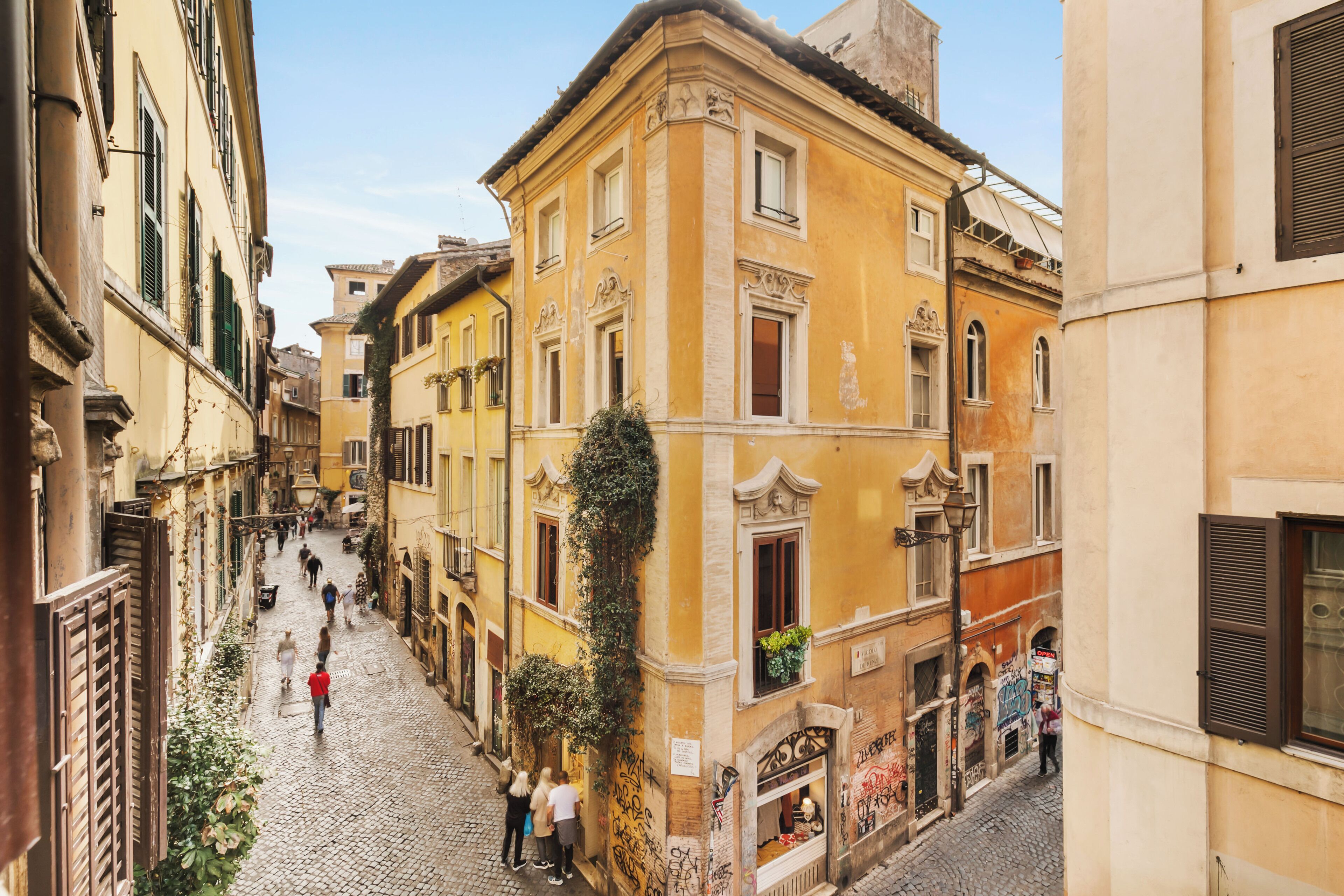A narrow cobblestone street lined with historic buildings, some with ivy and graffiti.