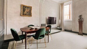 A dining room with a wooden table, green upholstered chairs, a painting on the wall, a television, and a statue. - Luxury apartment in Trastevere (Roma)