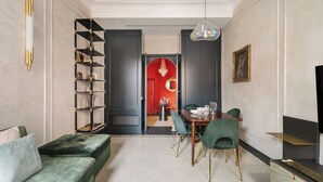 A modern living room with a green sofa, a dining table with chairs, a bookshelf, and a red accent wall. - Luxury apartment in Trastevere (Roma)