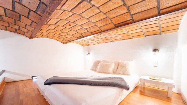 A bedroom with a sloped ceiling, a bed with white bedding, a bench, and a small table. - Best Location in Sayulita - Walk to Everything (Sayulita)