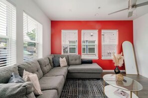 A living room with a sectional sofa, a glass coffee table, and a red accent wall.