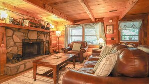 L’intérieur chaleureux d’un chalet avec une cheminée en pierre, des meubles en cuir et un plafond en bois rustique.