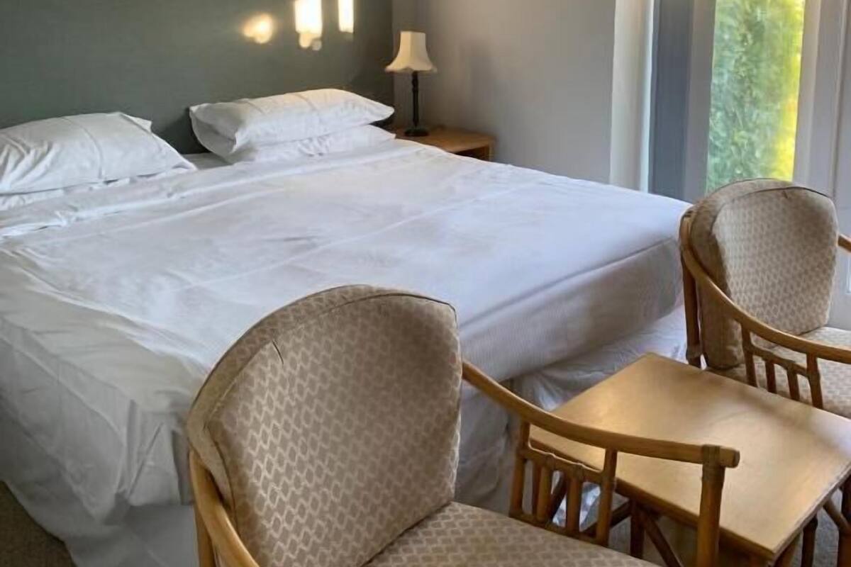 A hotel room with a large bed, two chairs, a small table, and a window with curtains.