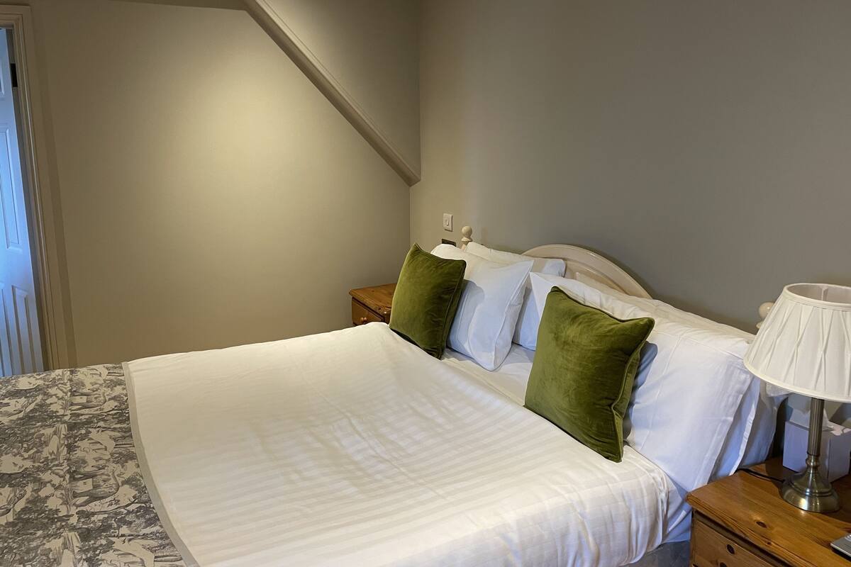 A neatly made bed with white linens and green pillows, a bedside lamp, and a wooden nightstand.