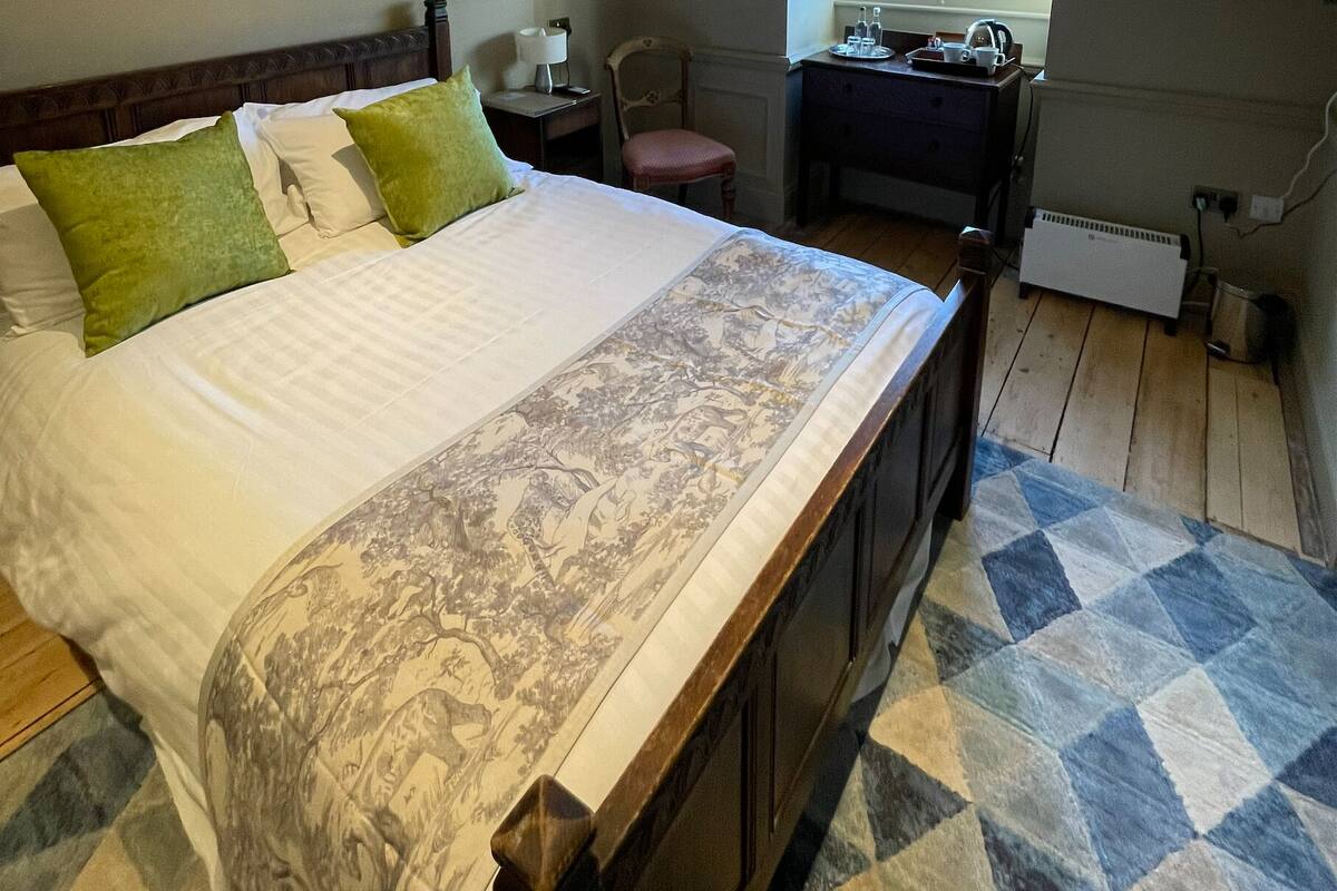 A bedroom with a large bed, a desk, a chair, and a radiator.
