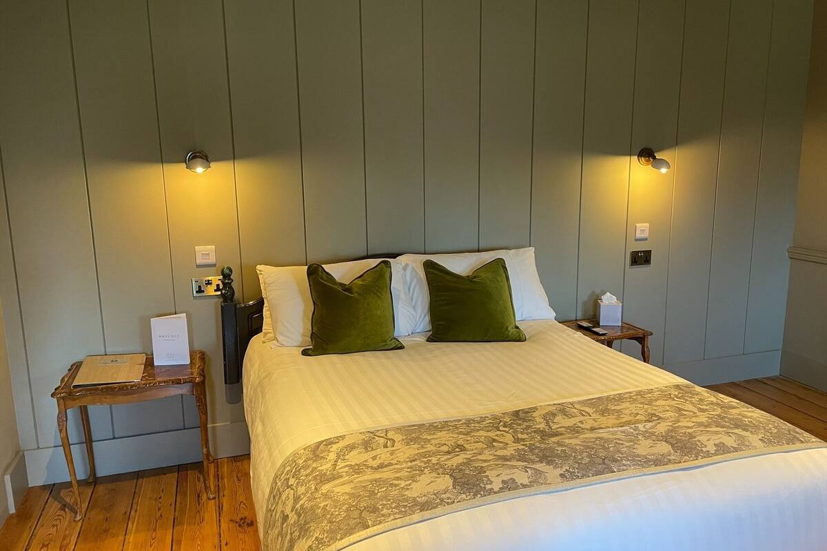 A neatly made bed with a patterned bedspread, two green pillows, and two wall-mounted lights.