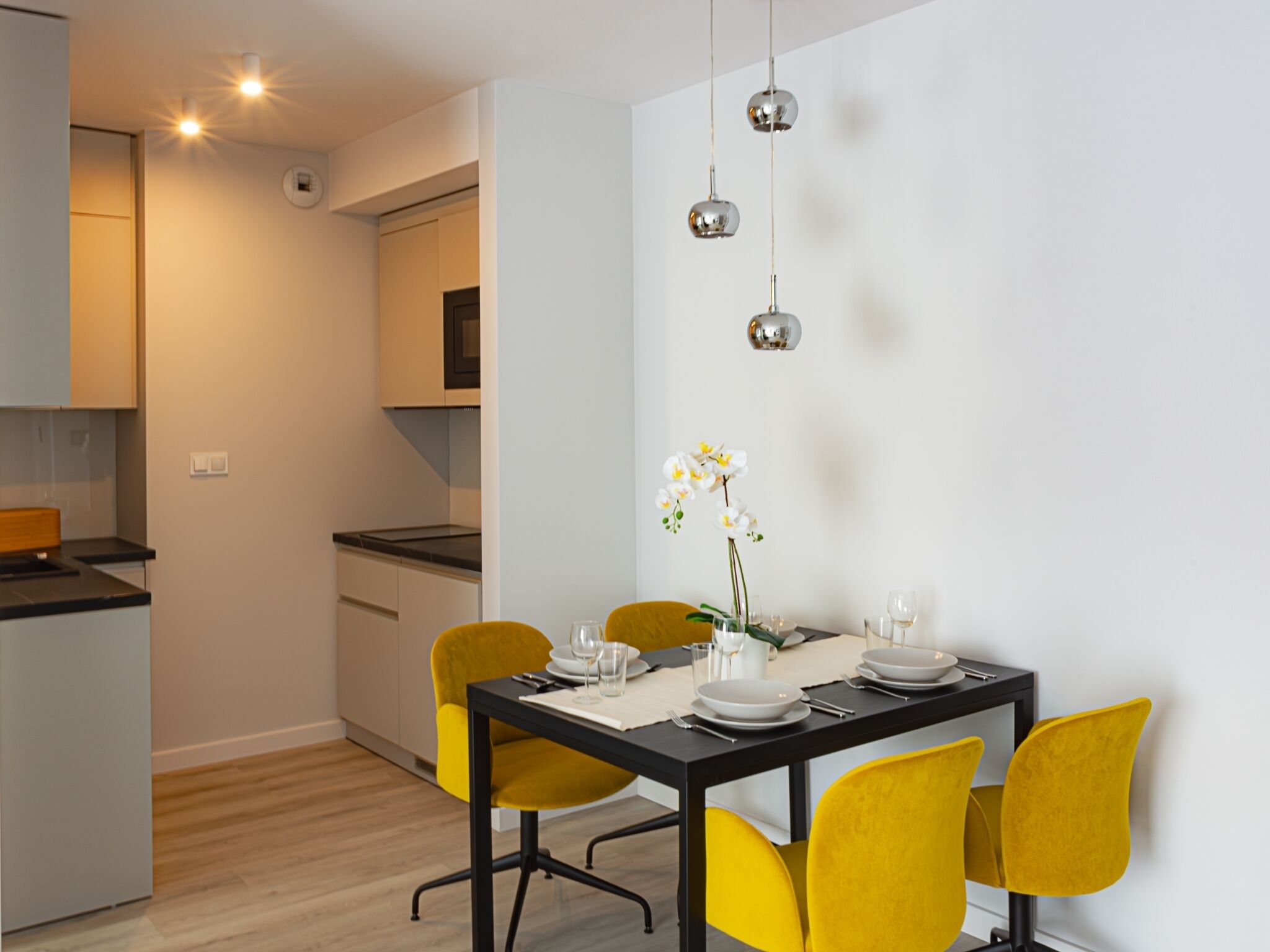 A modern dining area with a black table, yellow chairs, and a vase with white flowers.