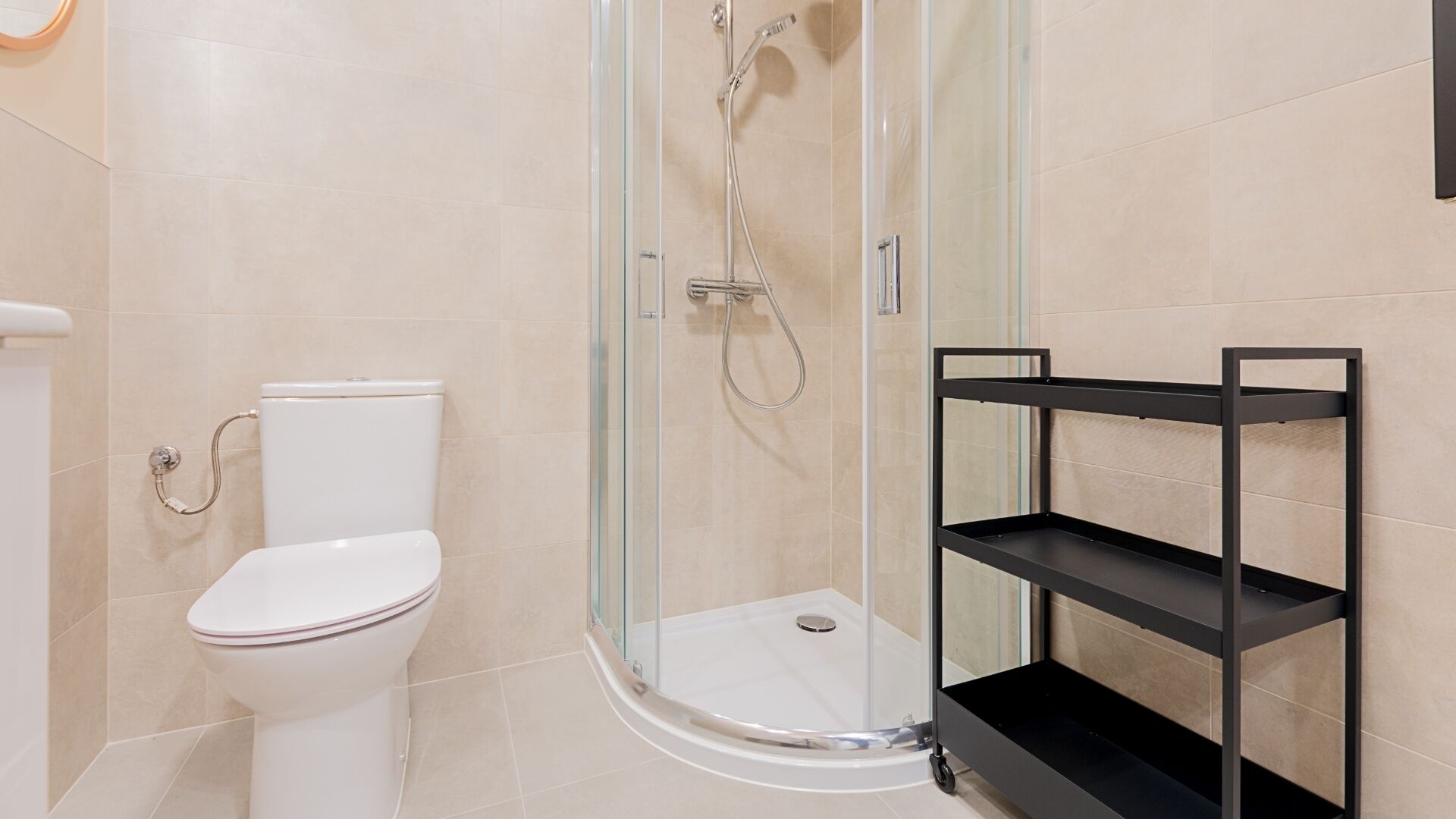 Un baño moderno con ducha de vidrio, inodoro blanco y estante de metal negro.
