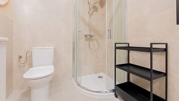 Un baño moderno con ducha de vidrio, inodoro blanco y estante de metal negro.