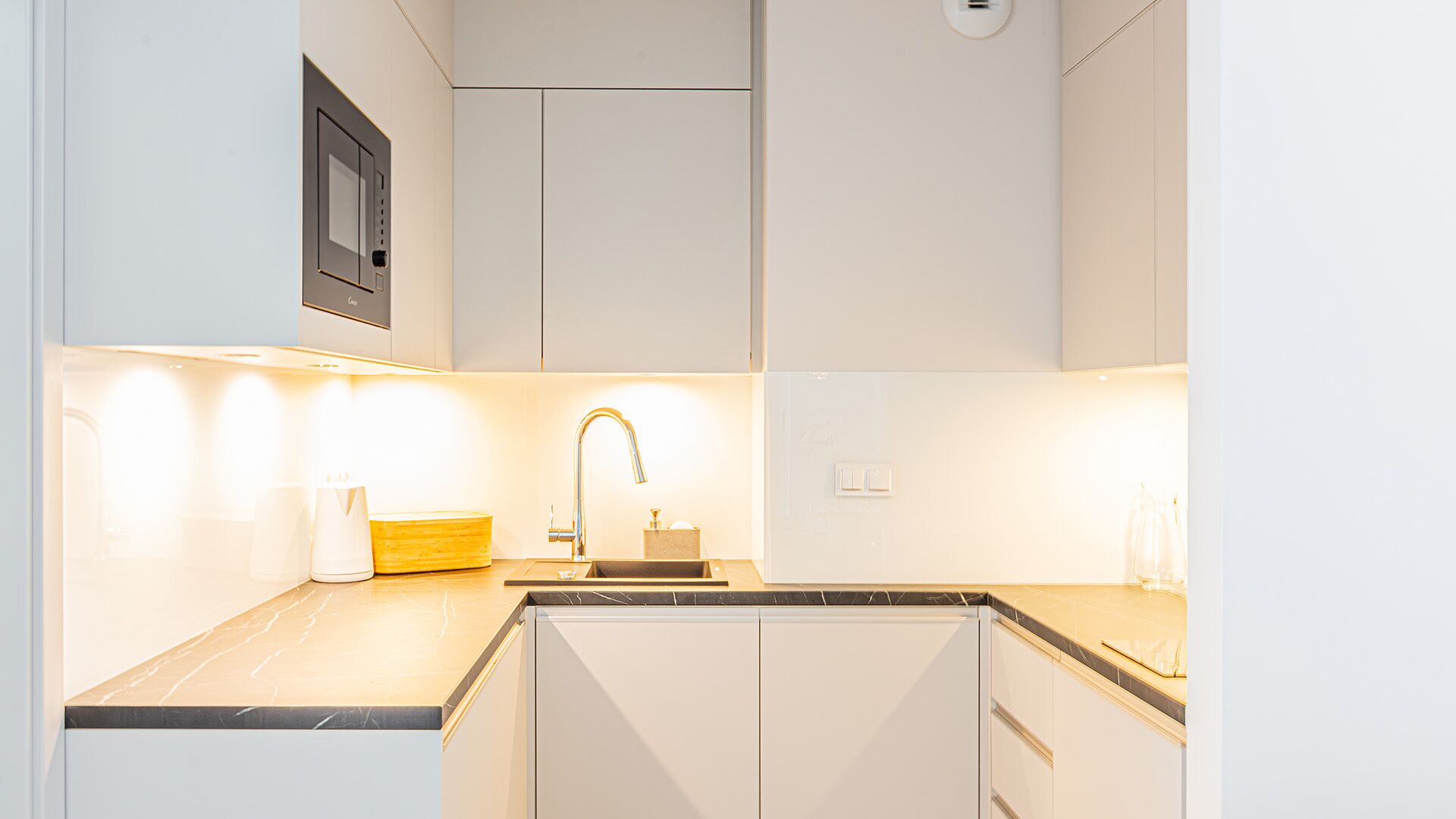 A modern kitchen with white cabinetry, a black countertop, and under-cabinet lighting.