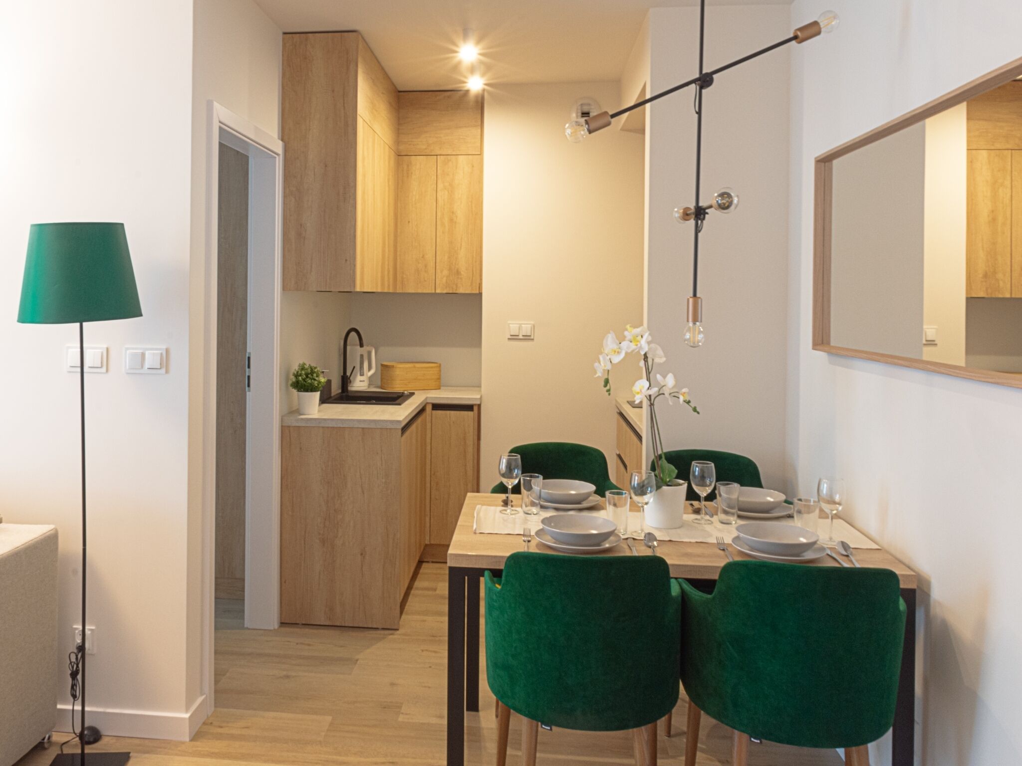 Una cocina moderna con armarios de madera, una mesa de comedor para cuatro personas y una lámpara de pie verde.