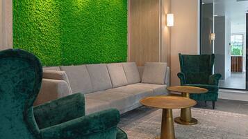 A modern lounge area with a green wall, a grey sofa, and two green armchairs with a small round table.