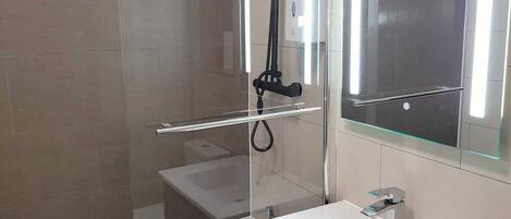 Une salle de bain moderne avec une douche à parois de verre, un lavabo blanc et un grand miroir.