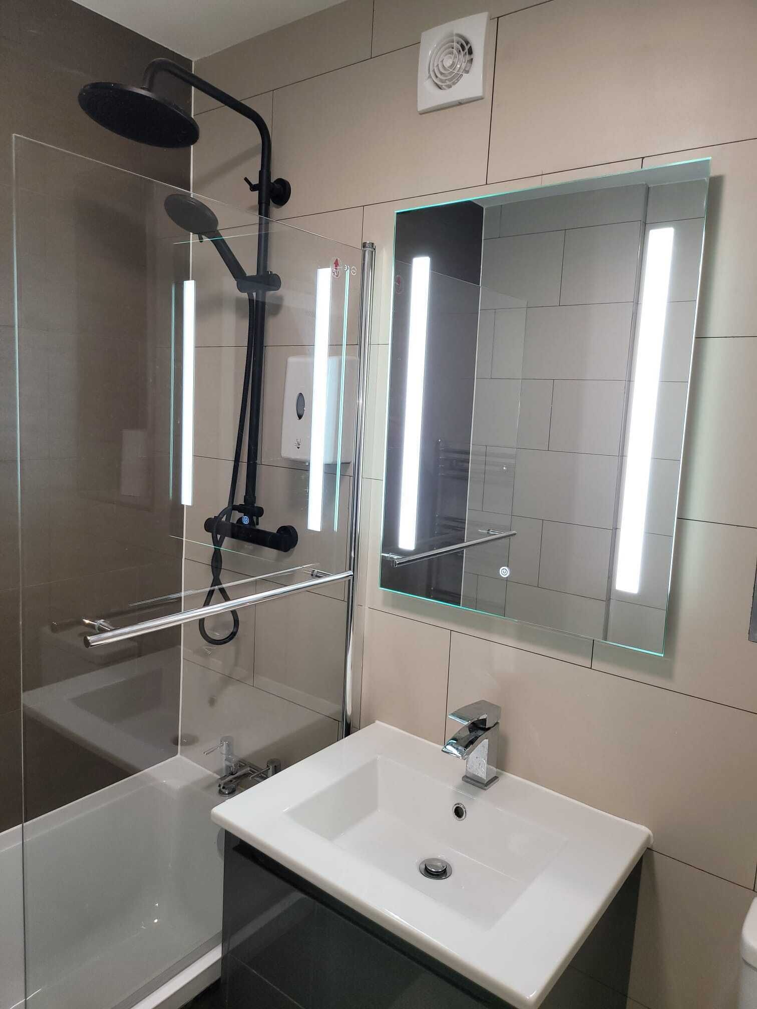 Une salle de bain moderne avec une douche à l’italienne en verre, un lavabo blanc et un grand miroir.