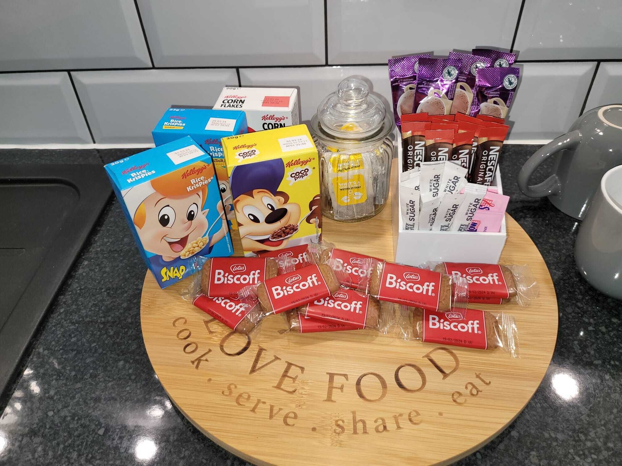A variety of food items including rice krispies, rice crispy treats, corn flakes, and biscotti on a wooden board with the text "LOVE FOOD eat cook serve share".