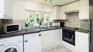 A modern kitchen with white cabinets, a dishwasher, a microwave, a toaster, and a bread maker.