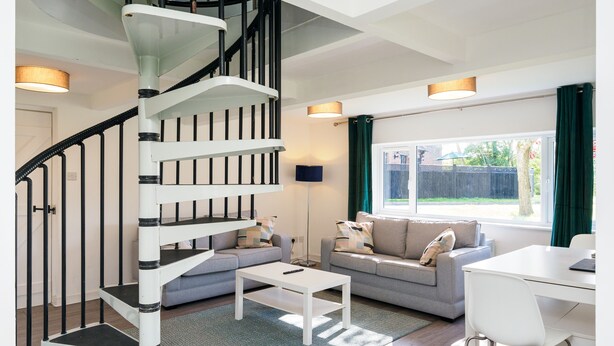 A modern living room with a spiral staircase, two sofas, a coffee table, and a dining area.