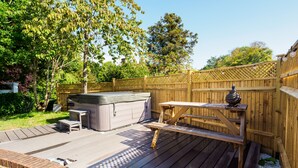 A wooden deck with a hot tub, picnic table, and steps leading to a covered area.