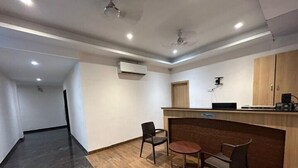 Un espace d’accueil comprenant un comptoir en bois, deux chaises, une petite table et un ventilateur de plafond.