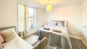 A bedroom with two beds, a window with curtains, a hanging light fixture, and a patterned rug. - 4 bed cottage (Contractors Welcome) Egham (Egham)