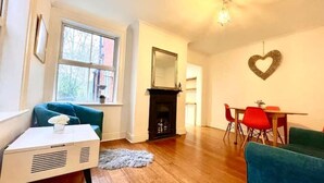 A living room with a fireplace, a dining area with red chairs, and a heart-shaped decoration on the wall. - 4 bed cottage (Contractors Welcome) Egham (Egham)
