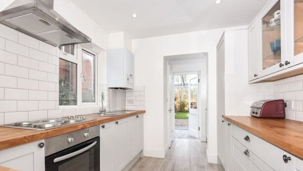 A modern kitchen with white cabinetry, a wooden countertop, and a view into the backyard. - 4 bed cottage (Contractors Welcome) Egham (Egham)