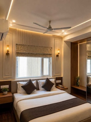 A bedroom with a large bed, a ceiling fan, wall sconces, and a window with blinds.