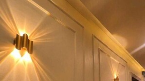 A hallway with wall-mounted lighting fixtures and a door. - Anaya Retreat (Varanasi)