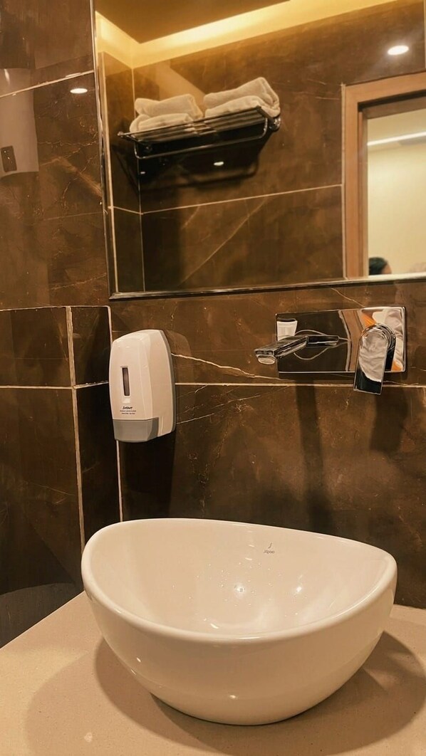 Une salle de bain avec un grand lavabo sur pied blanc, un distributeur de savon liquide et un porte-serviettes.