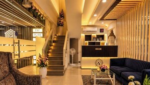 A hotel lobby with a reception desk, a staircase, a sofa, and a decorative Buddha statue. - Anaya Retreat (Varanasi)