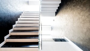 Una escalera moderna con barandilla de cristal que conduce a un rellano con pared de piedra.