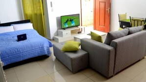 A hotel room with a bed, a sofa, a TV, and a small table. - Cheb's House (Abidjan)