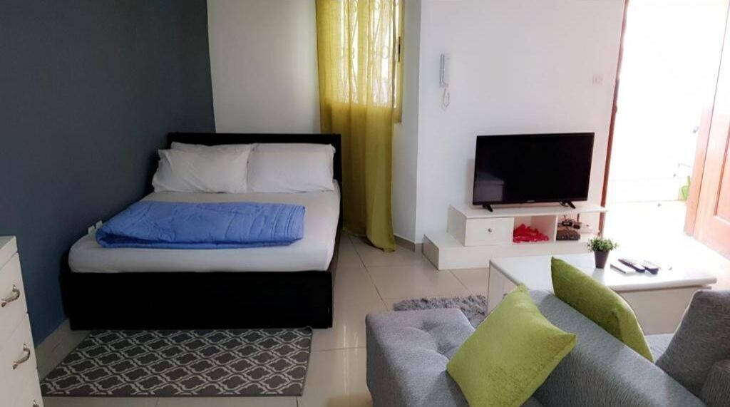 A bedroom with a bed, a TV, a small table, and a sofa.
