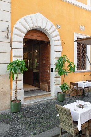 An outdoor seating area with a table and chairs, a potted plant, and a building entrance. - Passpartout Boutique Palace (Rome)