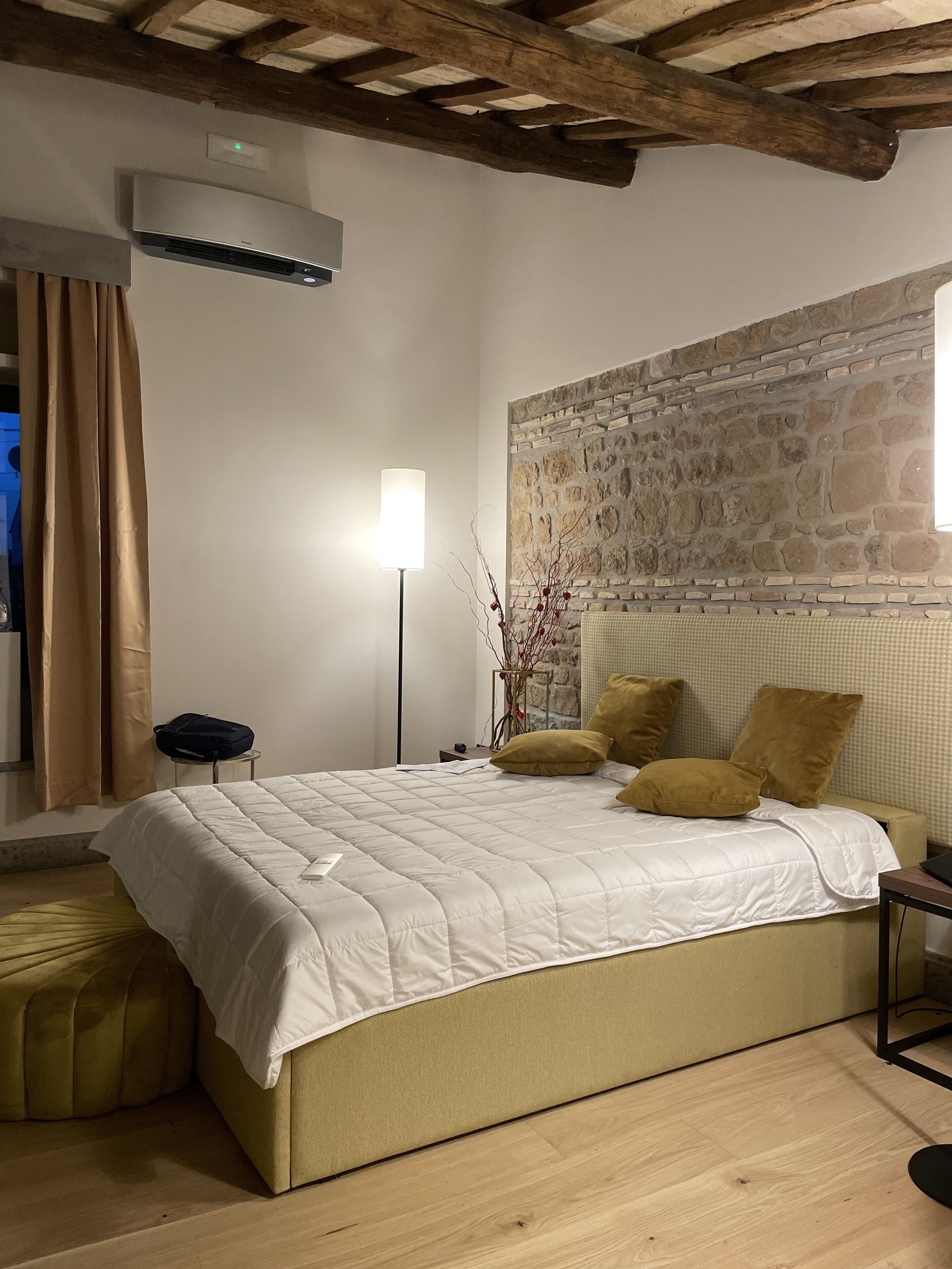 A bedroom with a stone wall, a bed with a white quilt, and a lamp.