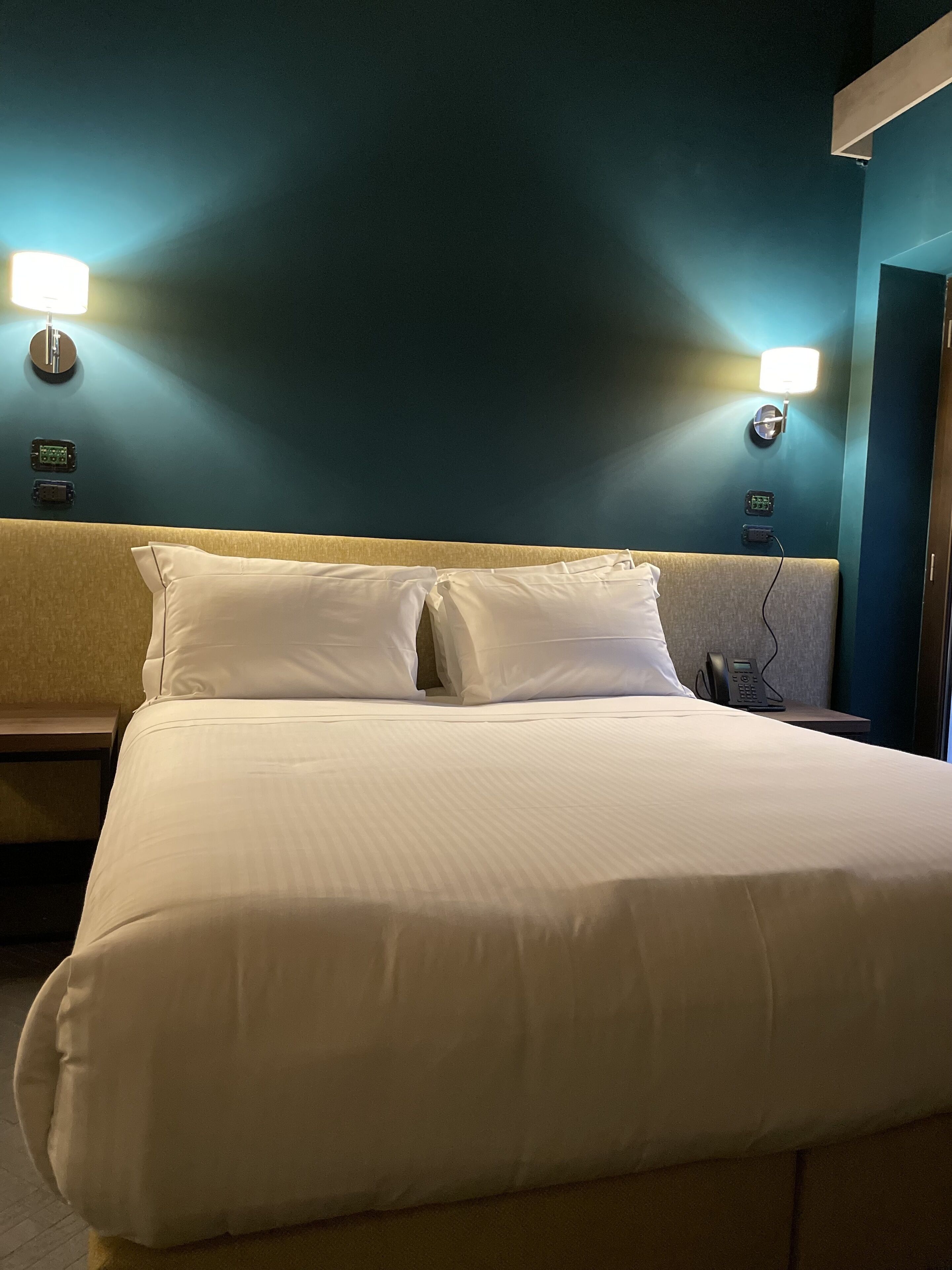 A hotel room with a bed, two bedside lamps, and a phone on the nightstand.