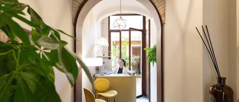 A reception area with a receptionist, a yellow chair, a lamp, and a vase with sticks.