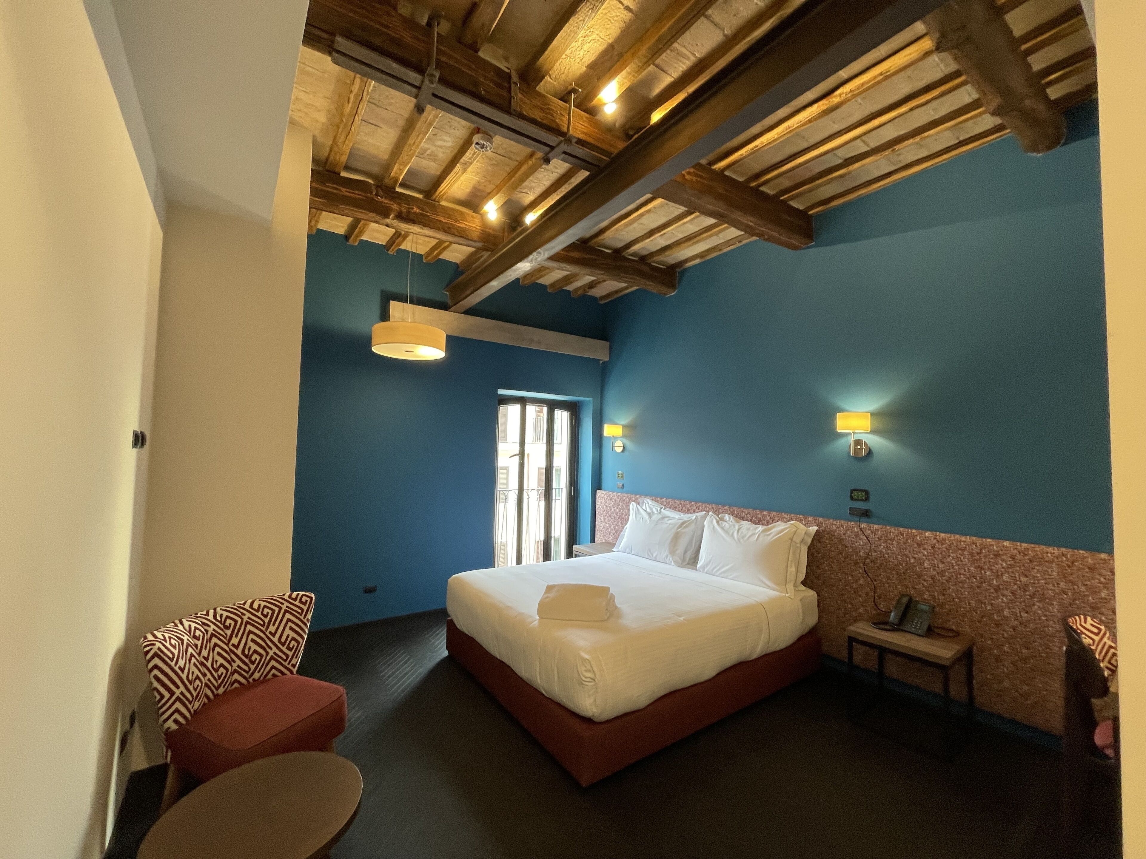 A hotel room with a large bed, a small table, a chair, and a window.