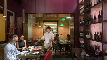 A restaurant interior with brick walls, wooden shelves with bottles, and diners at tables.